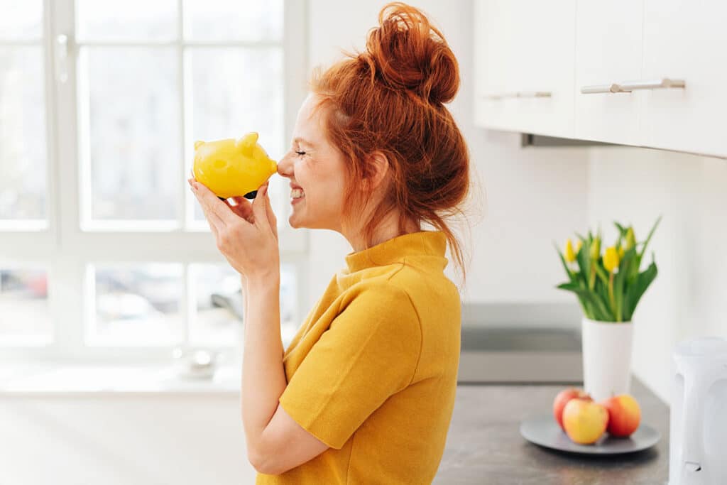Young woman smiling with a piggy bank touching her nose in relation to secondary rhinoplasty.