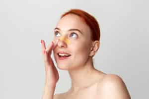 Young woman with a bandaid on her nose that represents recovery from a revision surgery that repaired the results of a previous surgery.
