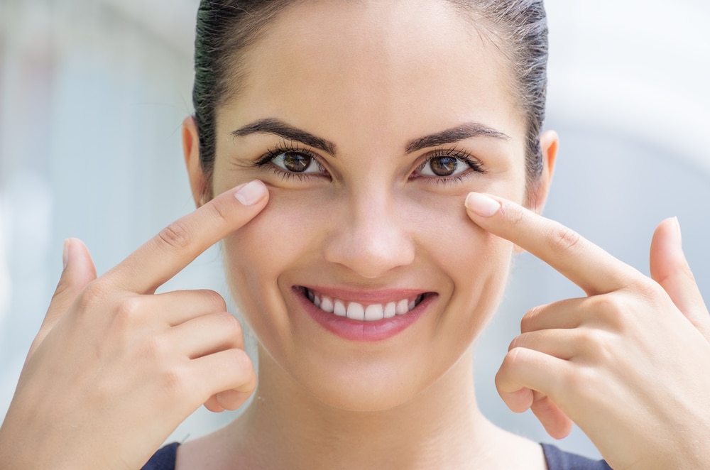 Smiling woman pointing to her infraorbital region, a sensitive area for precise Botox injections.