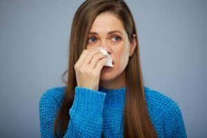 Woman with nasal drainage using a tissue after rhinoplasty, seeking relief from post-surgery symptoms.