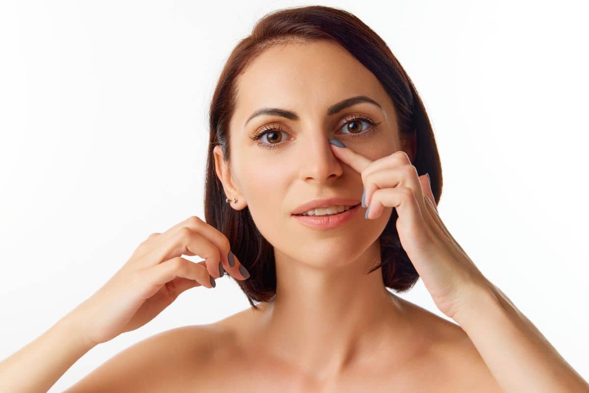 Woman gently touching her nose, illustrating timing considerations for revision rhinoplasty after initial surgery.