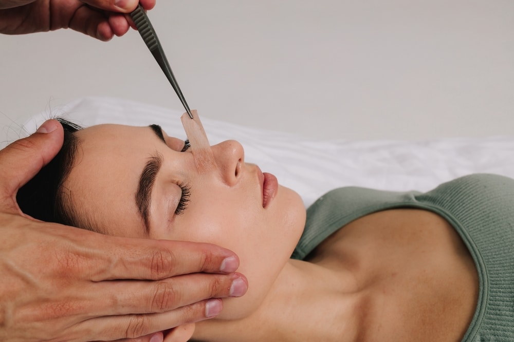 Surgeon examining woman's nasal structure with tool, highlighting considerations for multiple rhinoplasty procedures.