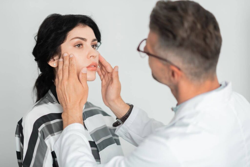 Surgeon examining patient’s face during follow-up visit after facial reconstructive surgery to monitor healing and recovery